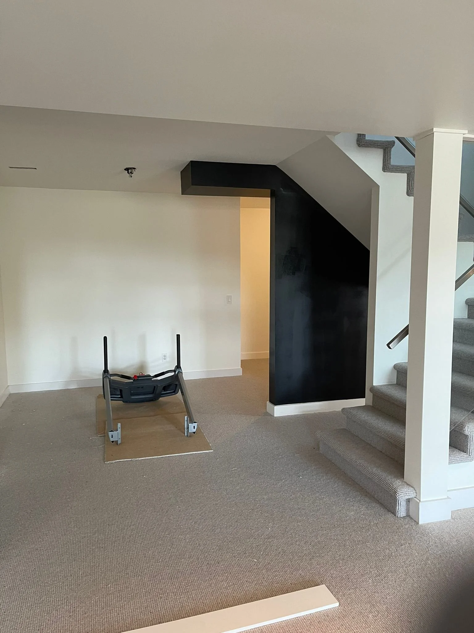 Room with staircase, beige carpet, black wall, partially assembled furniture, and a small platform on the floor.