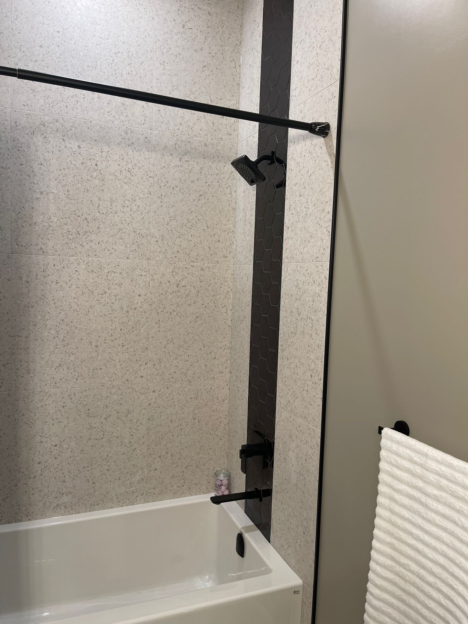 Bathroom with a bathtub, black shower fixtures, a handheld showerhead, and a rolled white towel on the right side of the image.