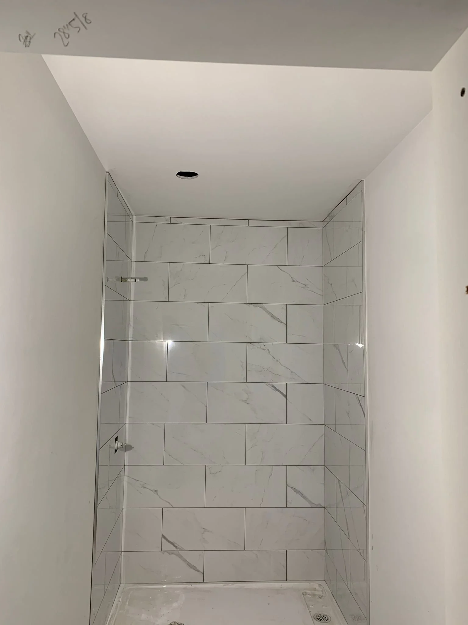 Empty bathroom shower area with white marble tiles and a small drain at the bottom right corner.