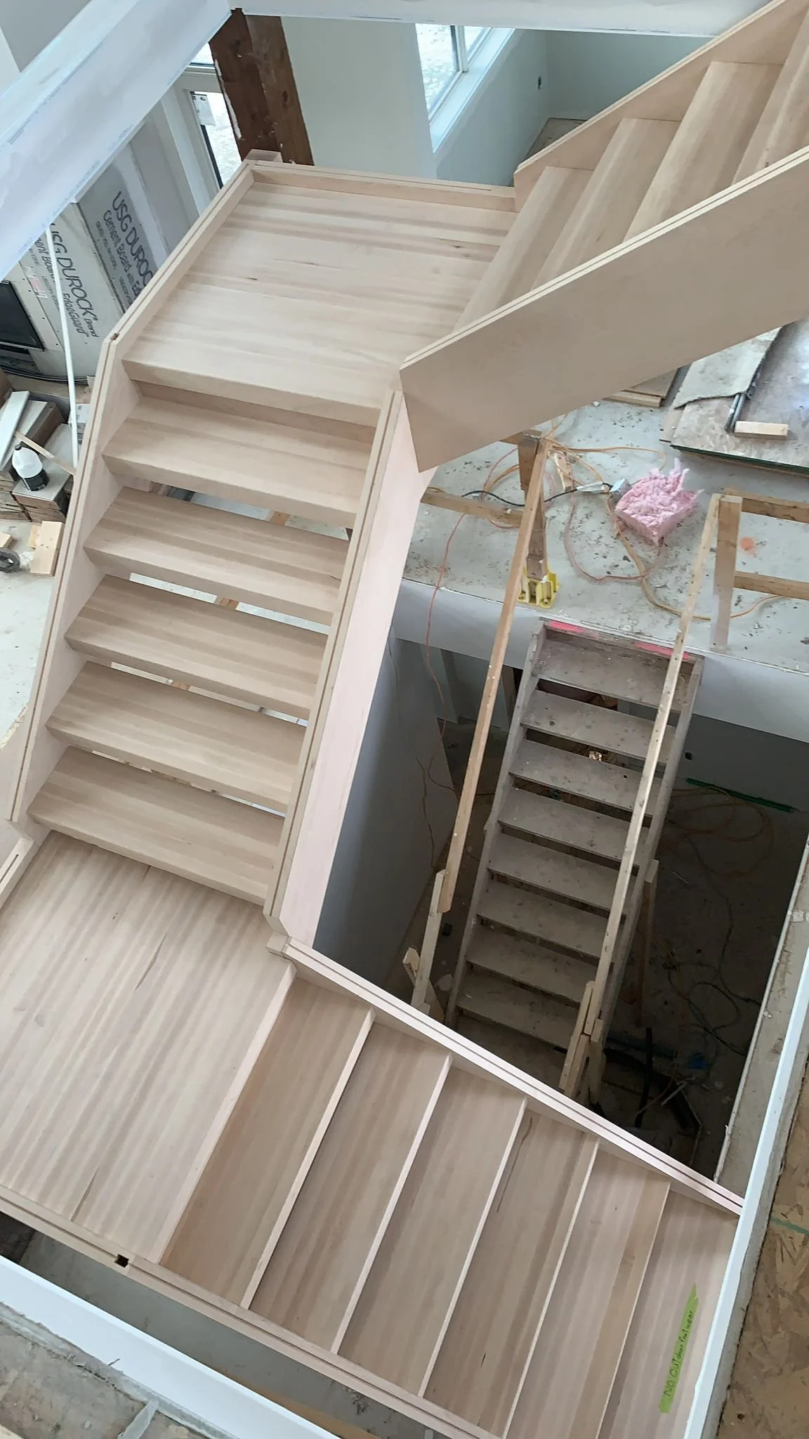 Indoor view of an unfinished staircase with wooden steps in a house under construction.