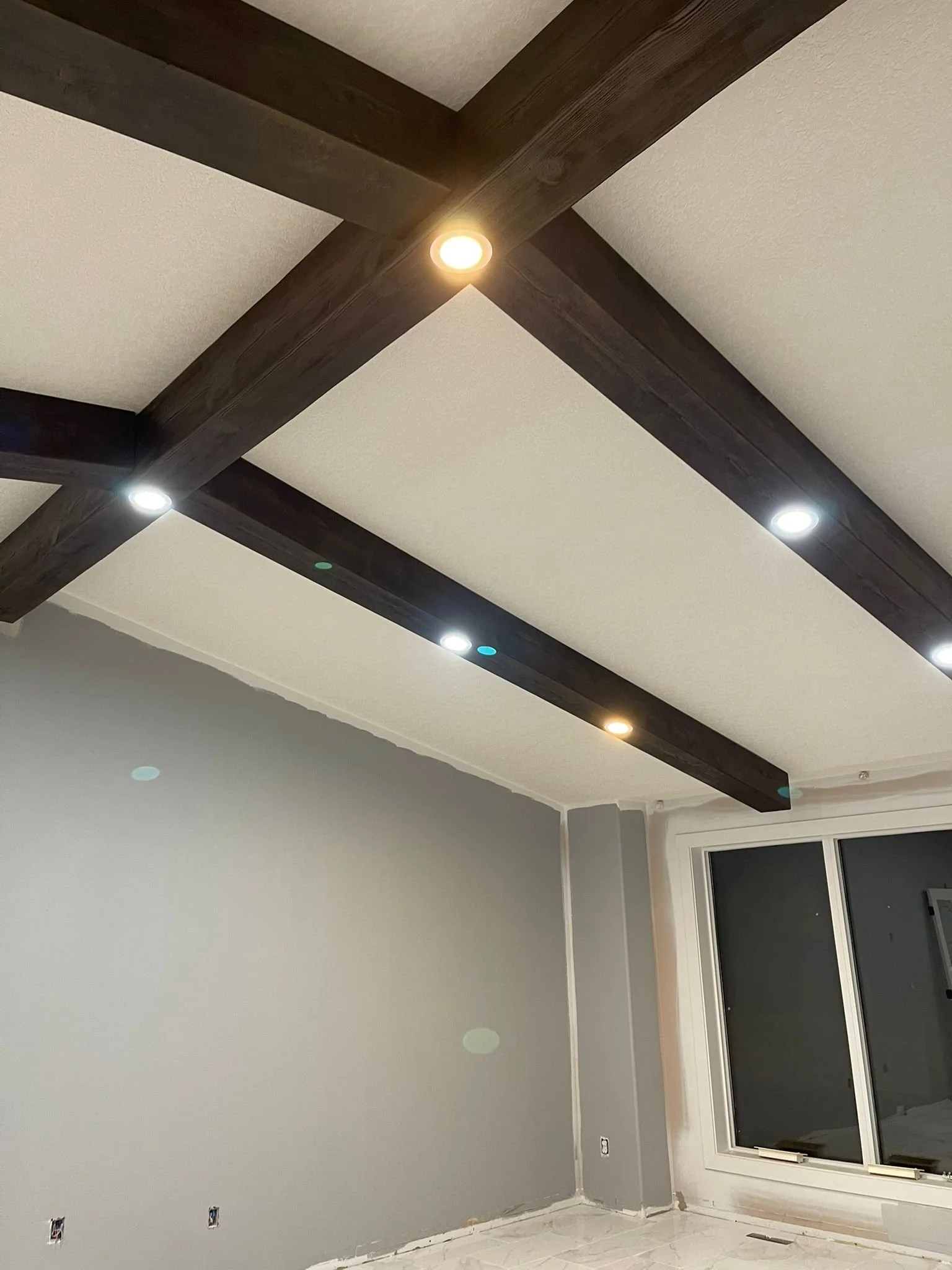 Interior room with gray walls, white baseboards, a large window with a sliding glass door, and dark wooden beams on the ceiling with built-in lights.