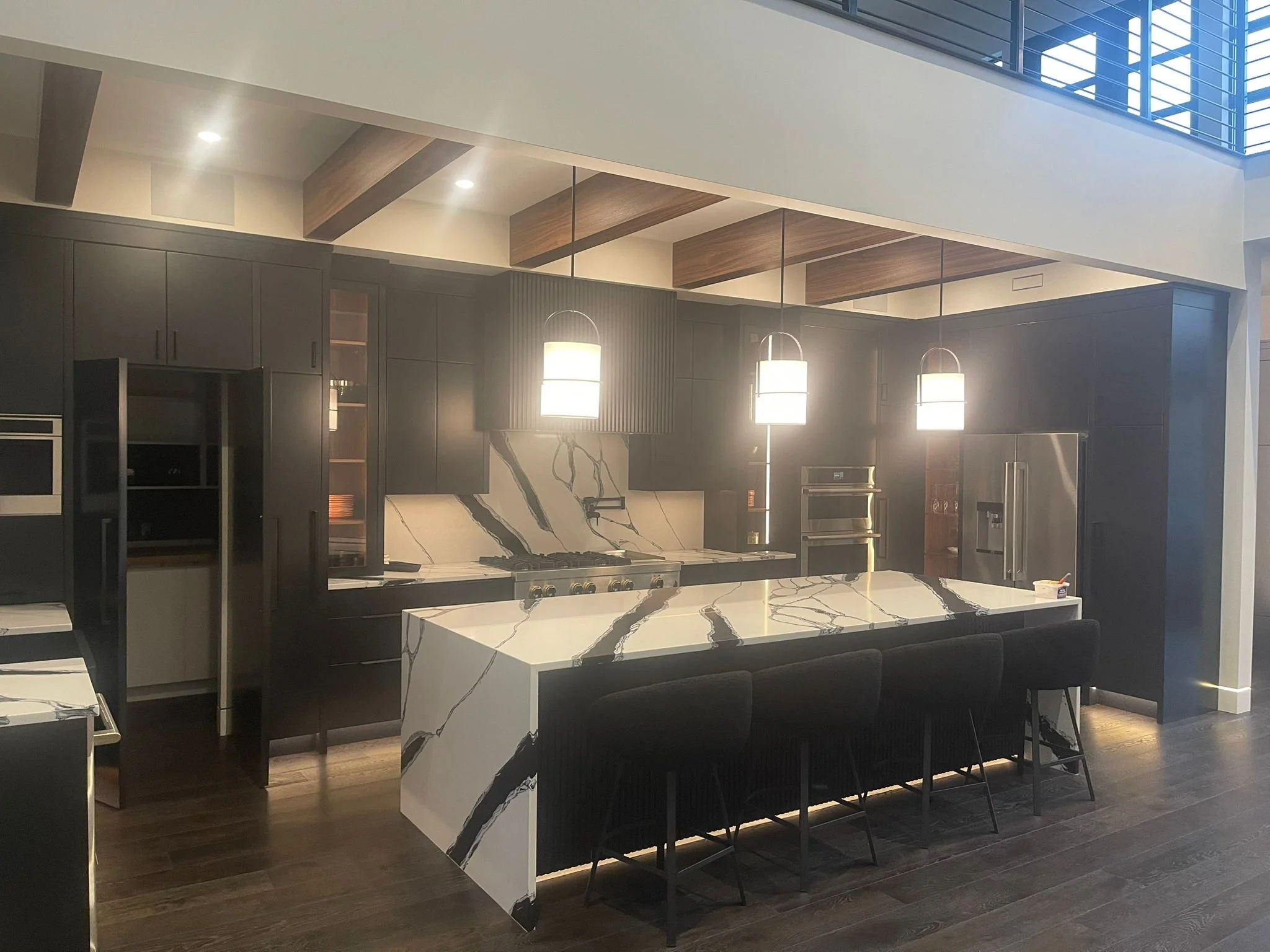 Modern kitchen with dark cabinets, marble island, and pendant lighting.