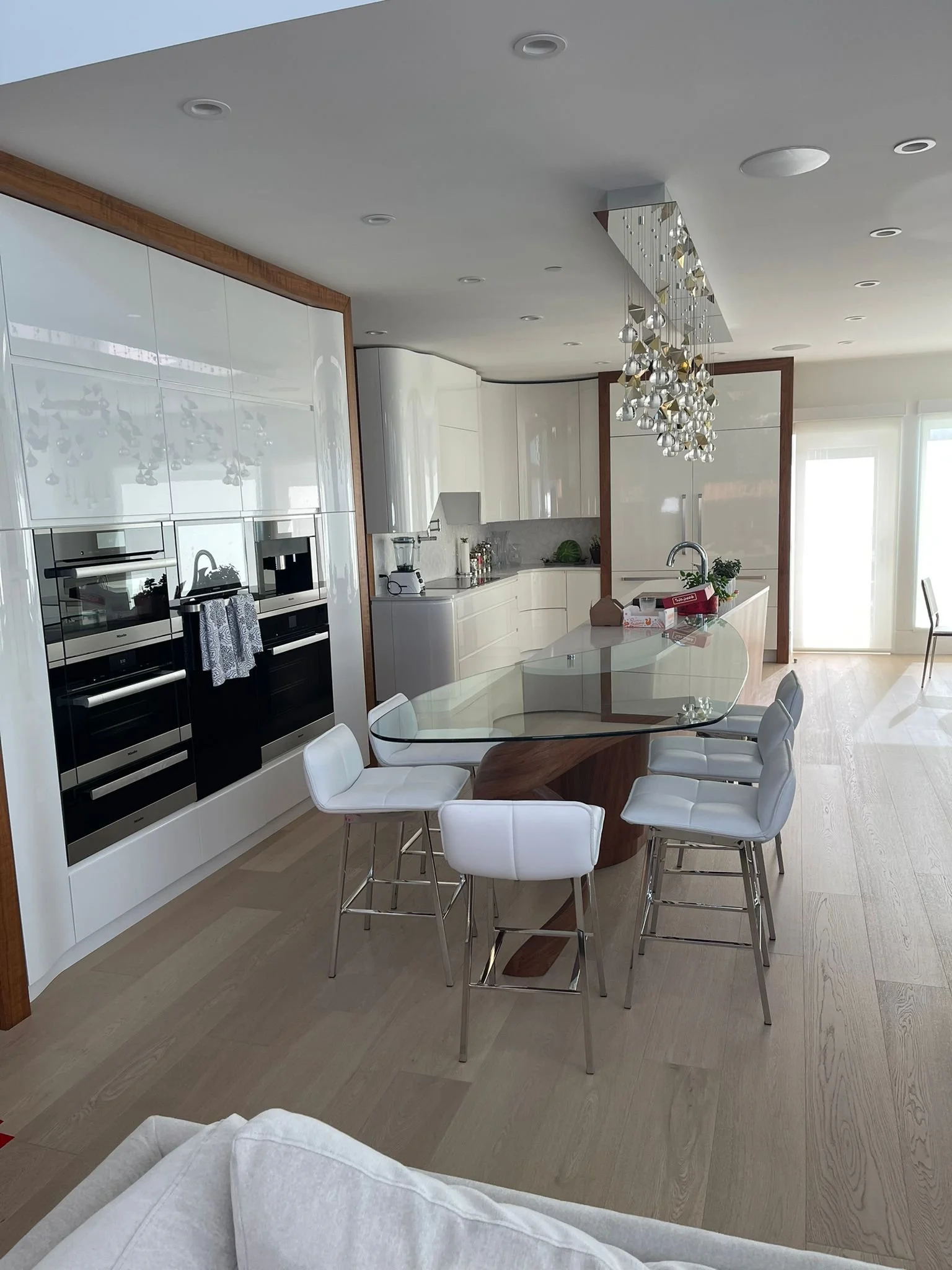 Modern kitchen with white cabinetry, a glass dining table, white chairs, and a chandelier hanging from the ceiling.