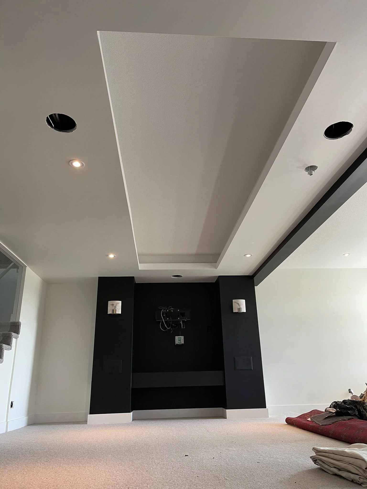 Image of a partially finished or renovated room with a black wall and a large white recessed ceiling area with multiple holes for lighting fixtures.