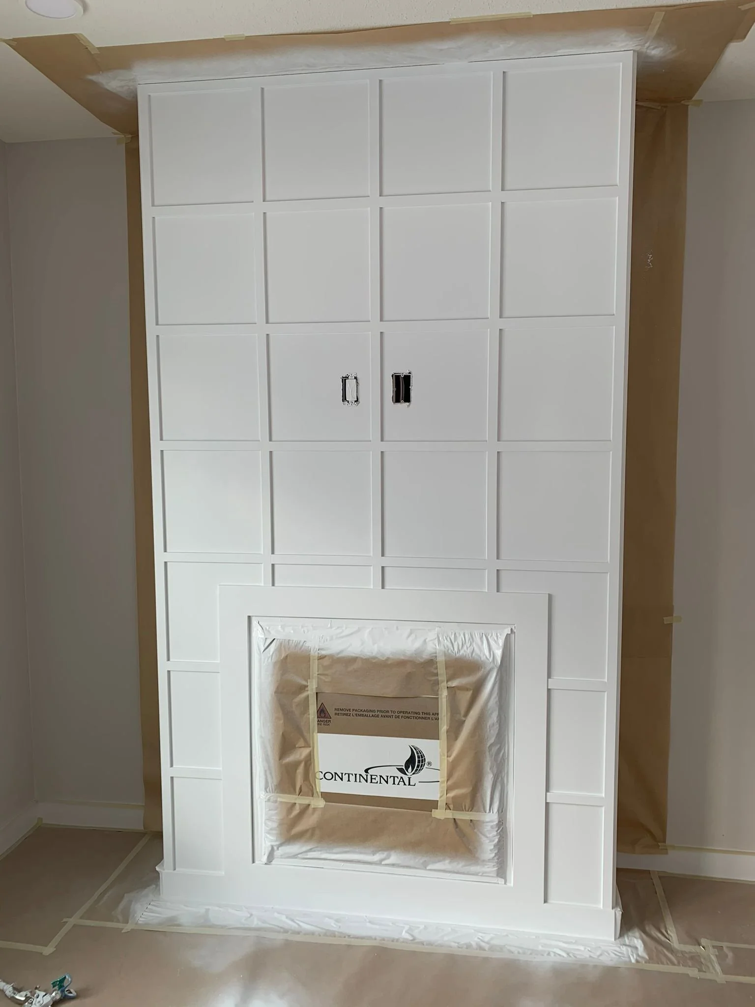 Interior of a room with a newly built white fireplace surround and cabinet. The fireplace opening is covered with a tan paper bag with a Continental logo, indicating ongoing construction or renovation.