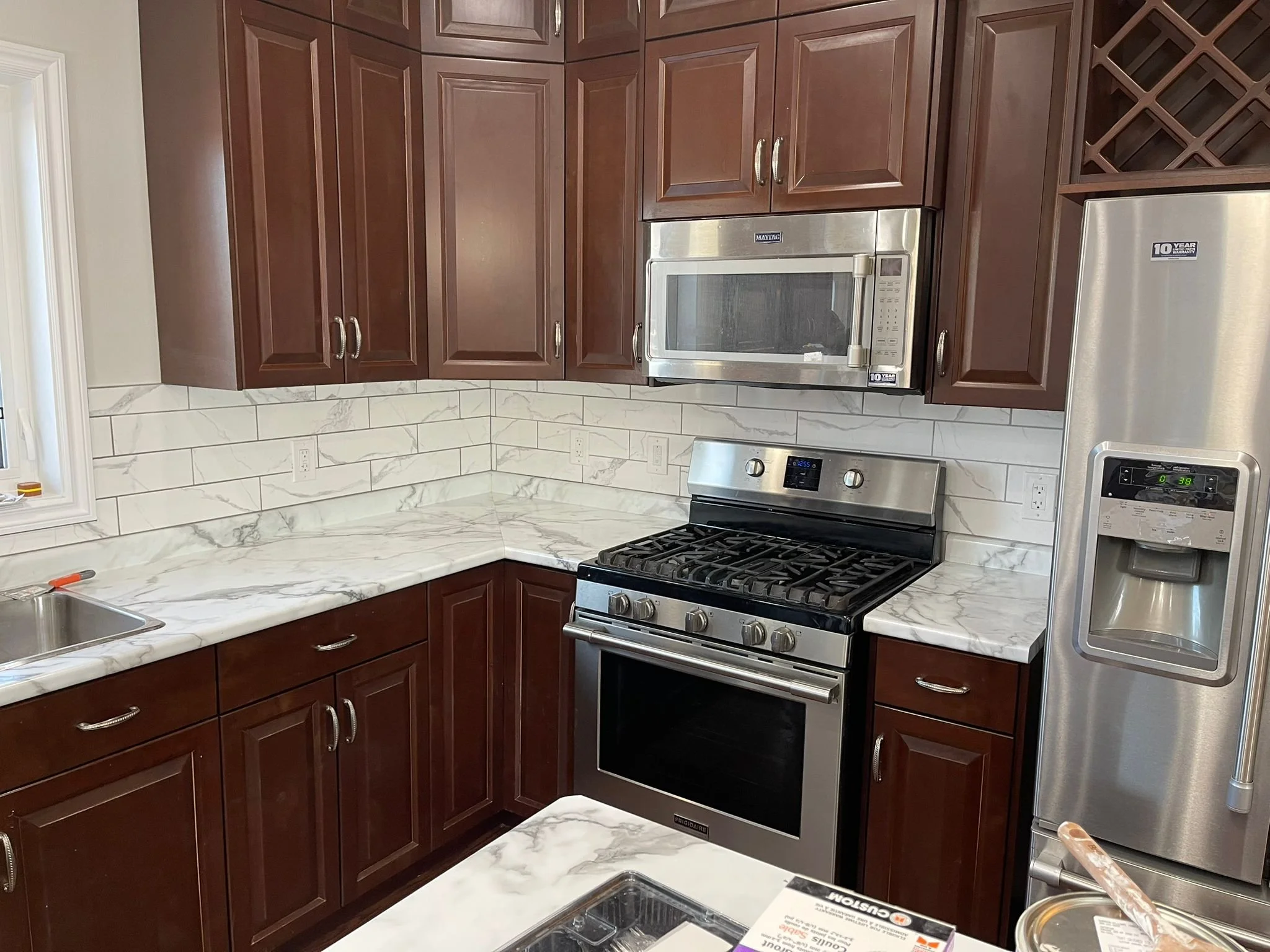 Kitchen with dark wood cabinets, white marble countertops, stainless steel microwave and oven, and a stainless steel refrigerator.