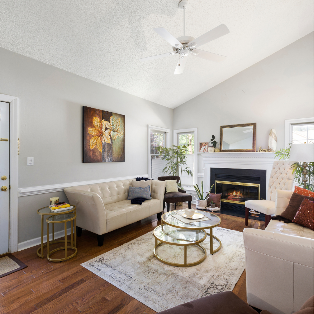 Living room with white sofas, a black fireplace, a round glass top coffee table, a ceiling fan, and decorative plants.