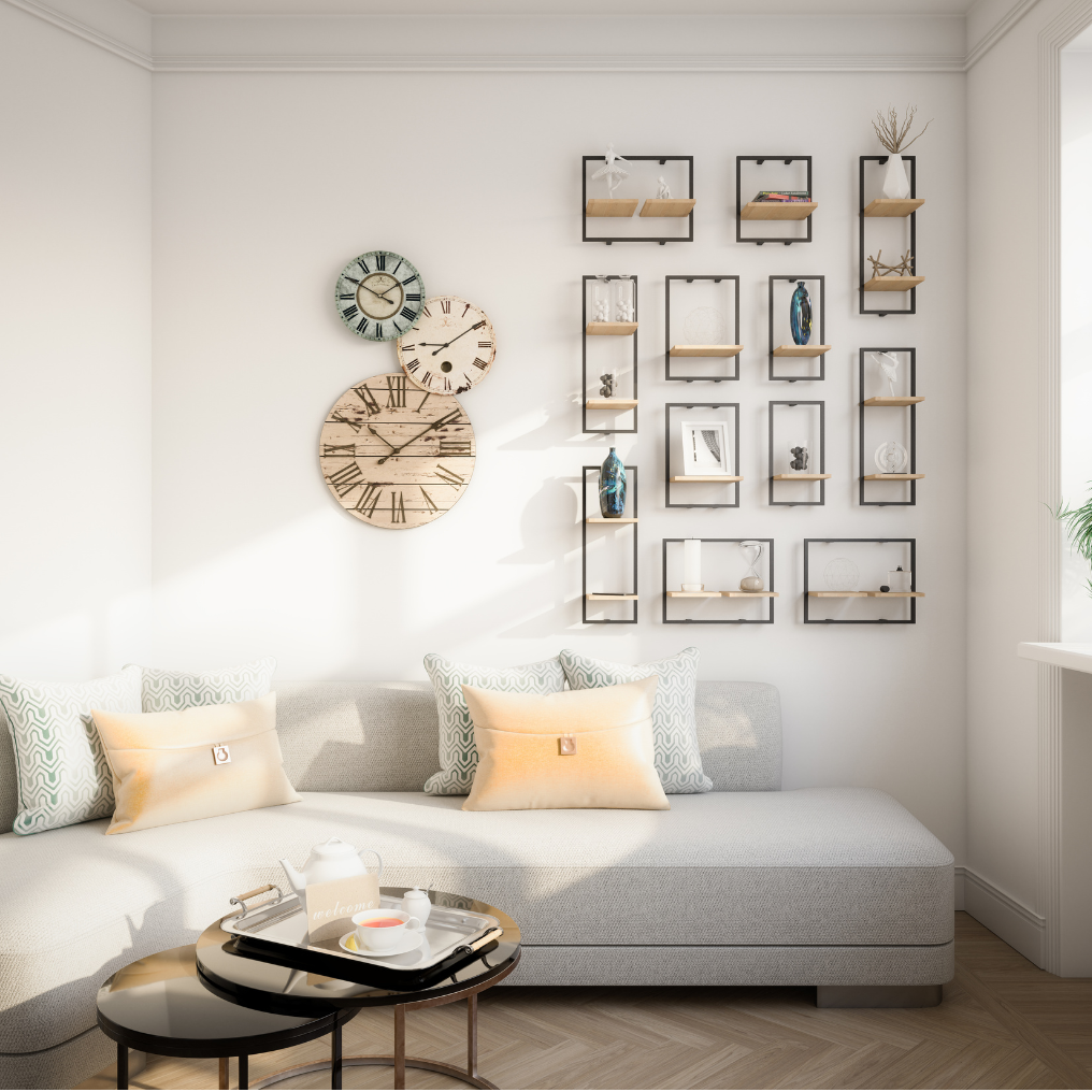 A cozy living room with a light gray sofa, beige and patterned throw pillows, and a small round black and gold coffee table with a tea set and a welcome sign. The wall features three rustic wooden clocks and a modern wall display with picture frames and decorative objects. Natural light streams in from a window on the right.