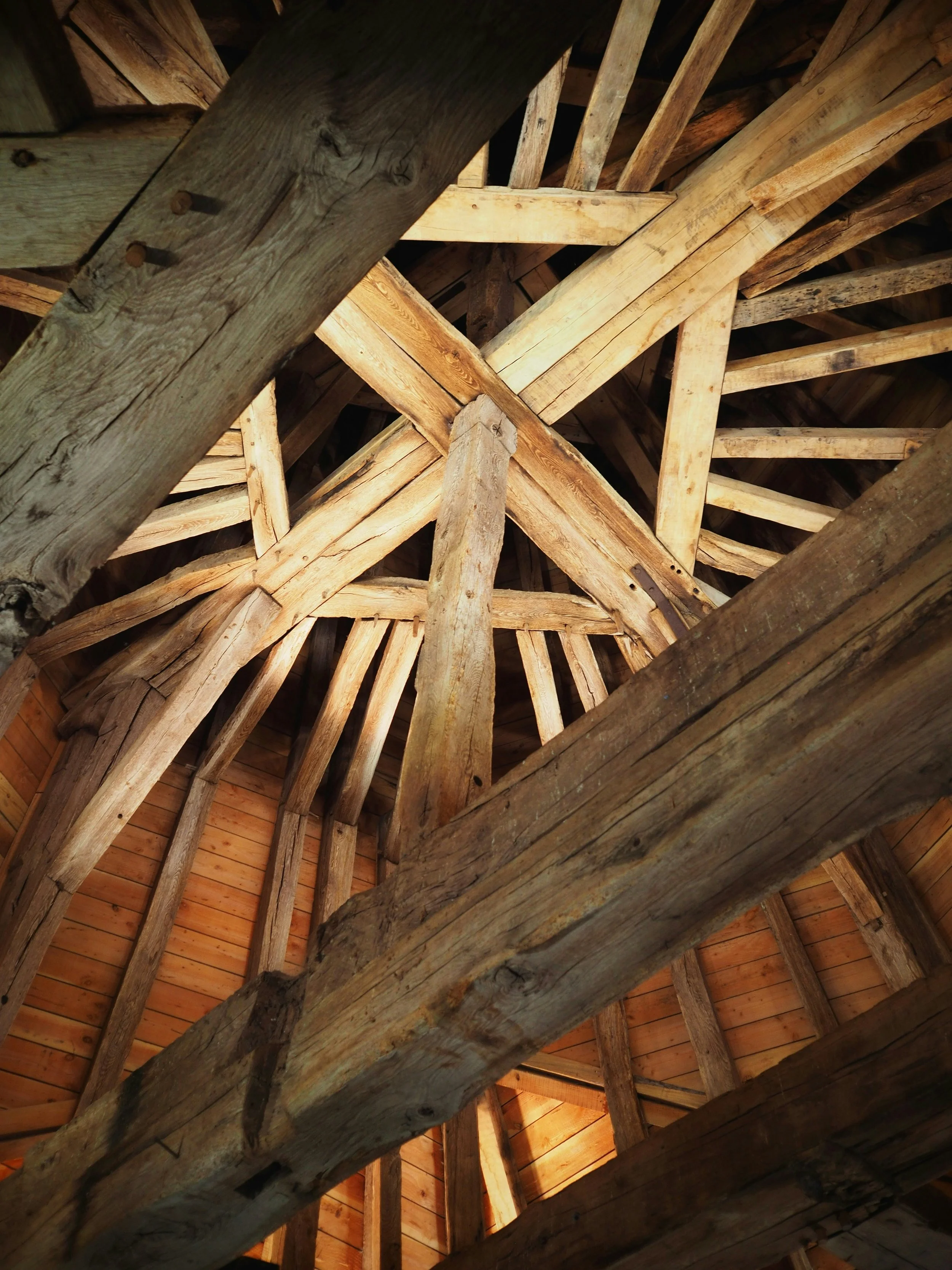 Wooden beams and rafters forming the ceiling of a barn or attic with natural wood color and texture.