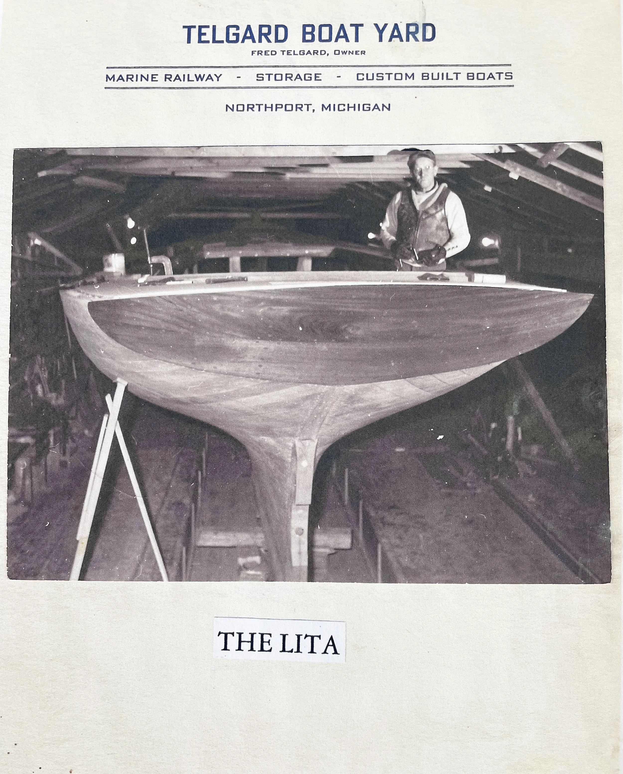 Old black and white photograph of a boat in a wooden workshop with a man standing behind it, the image is part of a display with text labels titled "TELGARD BOAT YARD" and "THE LITA."