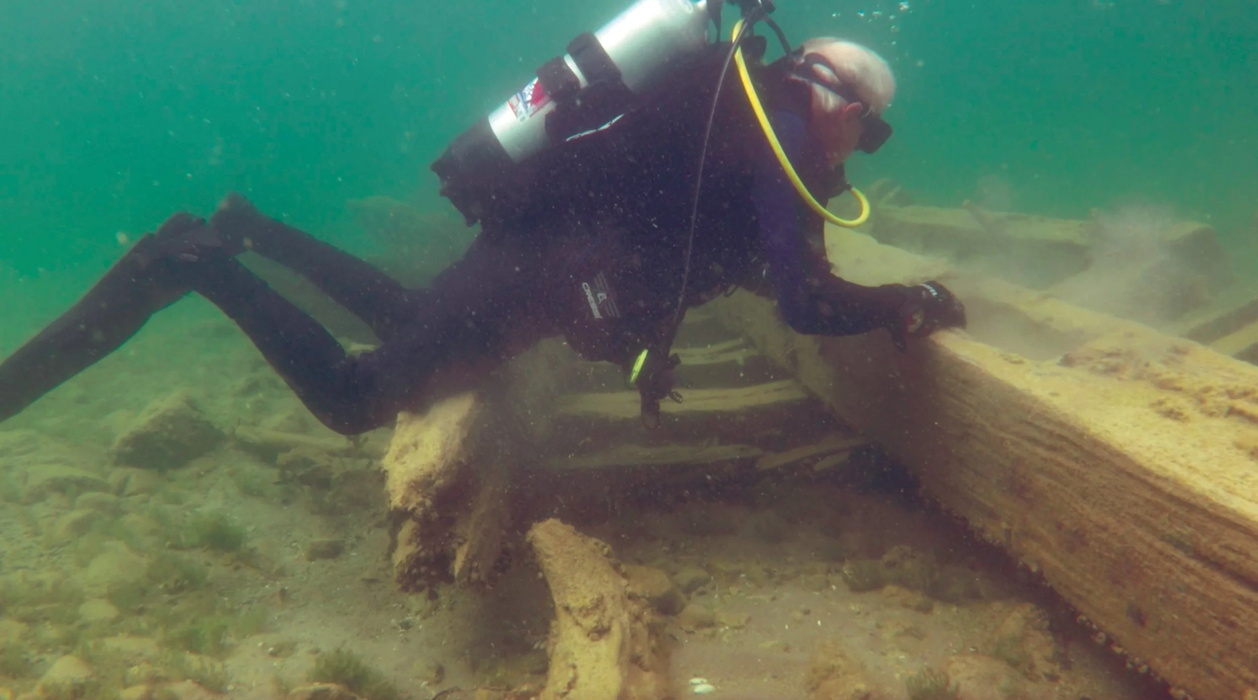 Scuba diver examining a sunken wooden structure underwater.