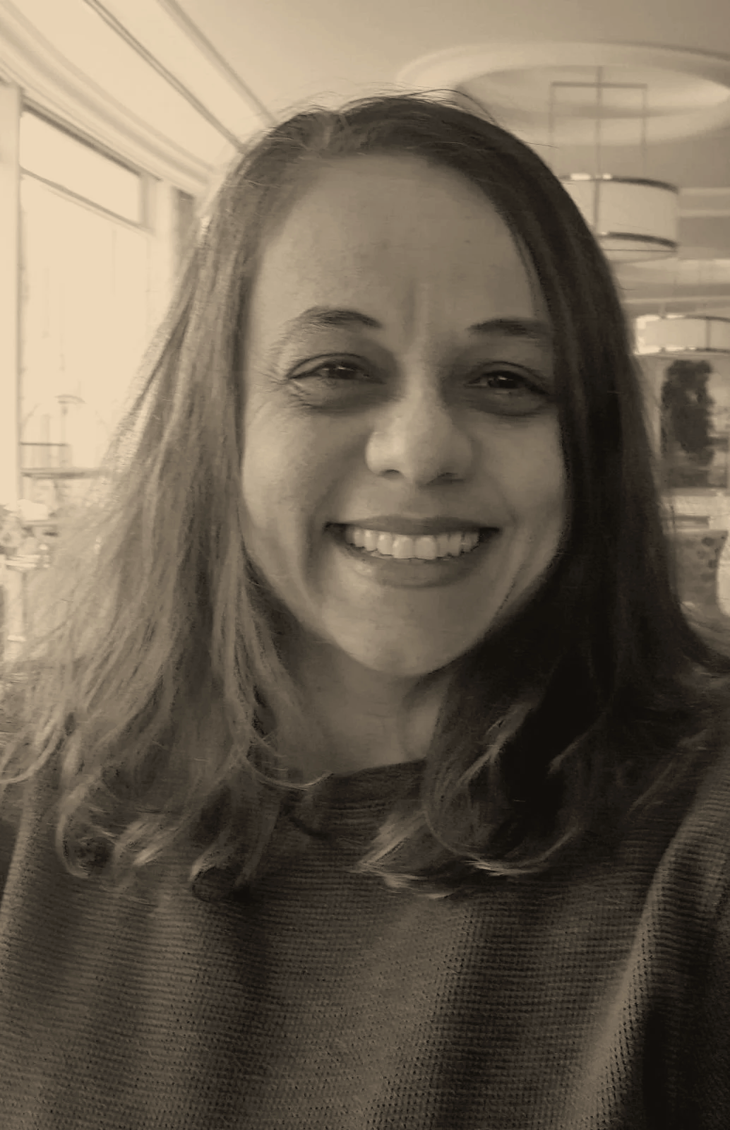 Valerie Calabria, the virtual office assistant for Vibrant Naturopathic Care has long hair in an indoor setting, with large windows and modern ceiling lights.