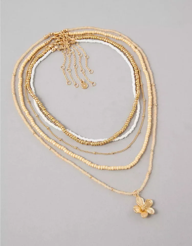 Multiple layered gold and white beaded necklaces on a gray background, with a butterfly pendant on the bottom necklace.