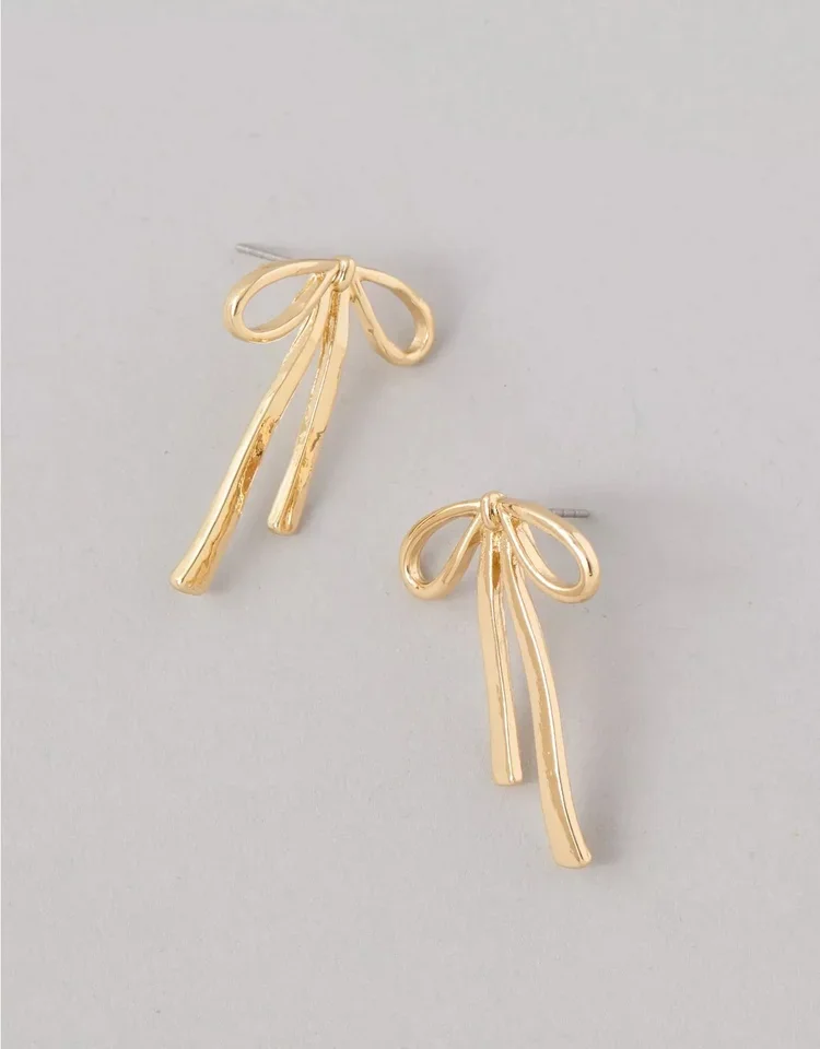 Gold earrings shaped like bows with dangling ribbon-like strands.