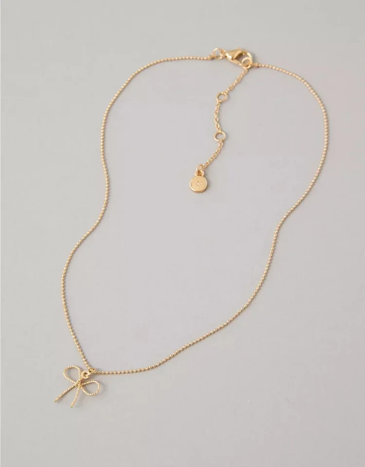 Gold necklace with a bow pendant and a small dangling charm with a heart