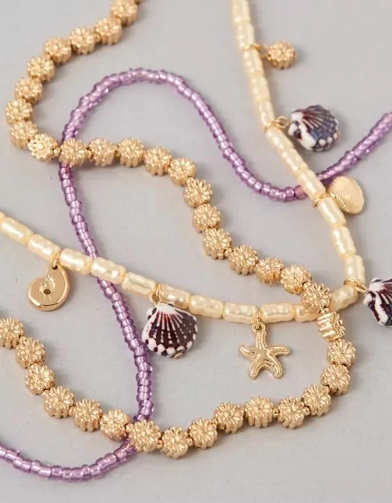 Several jewelry necklaces featuring gold, pearl, and purple beads, with shell and starfish charms.