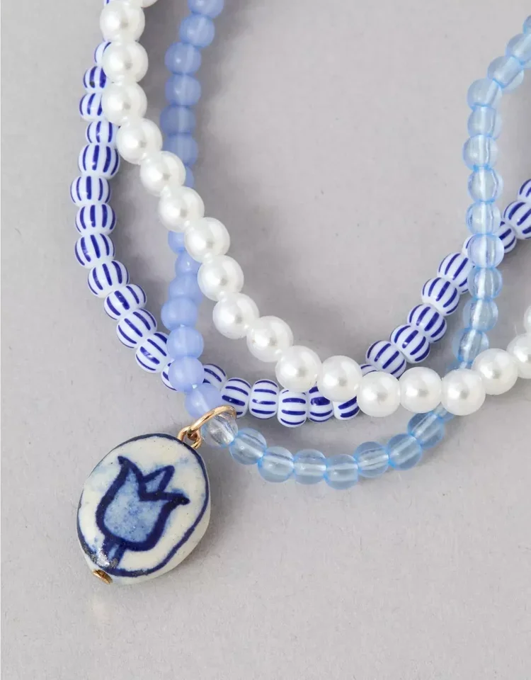 Close-up of three beaded necklaces in white and blue, with a ceramic pendant featuring a blue tulip design on a white background.