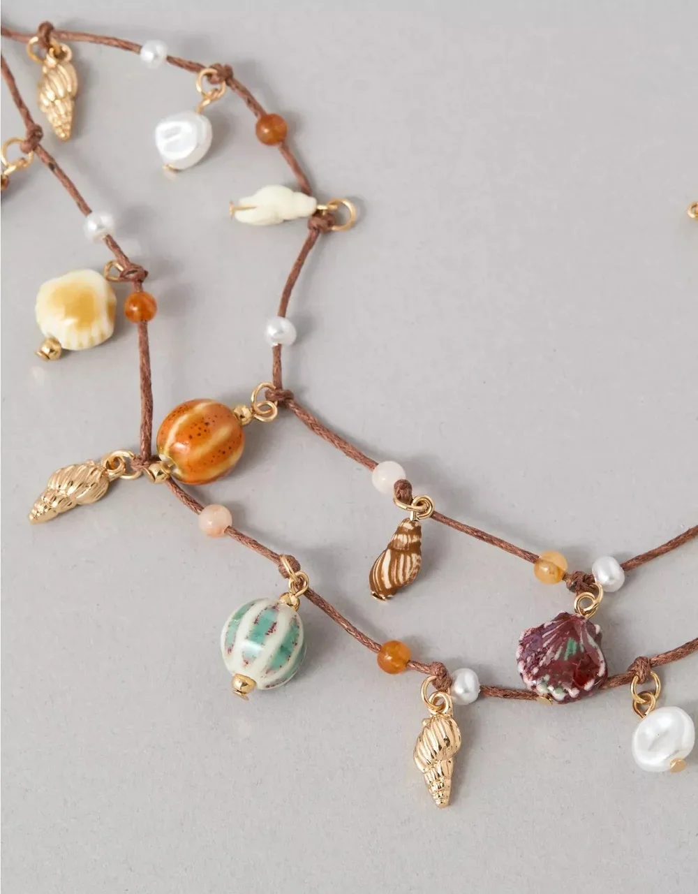 Close-up of a layered necklace with seashell charms, pearl beads, and small beads on brown cord.