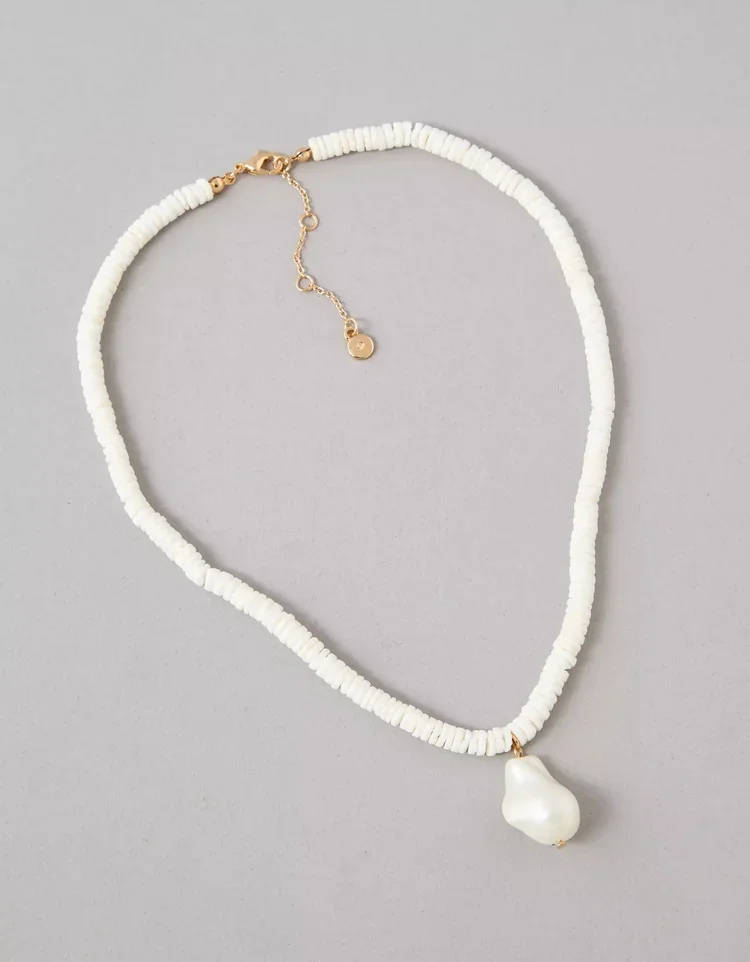 White bead necklace with a large baroque pearl pendant and a gold clasp, laid out on a gray background.