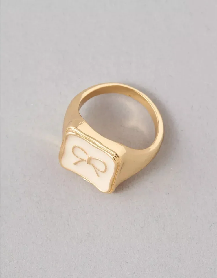 Gold ring with a white rectangular face featuring a small gold bow design.