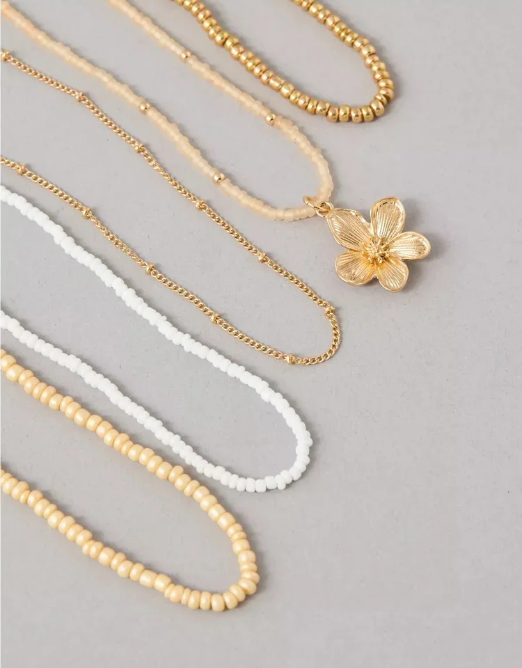 Assorted beaded necklaces in gold, white, and cream colors, with one featuring a large gold flower pendant.
