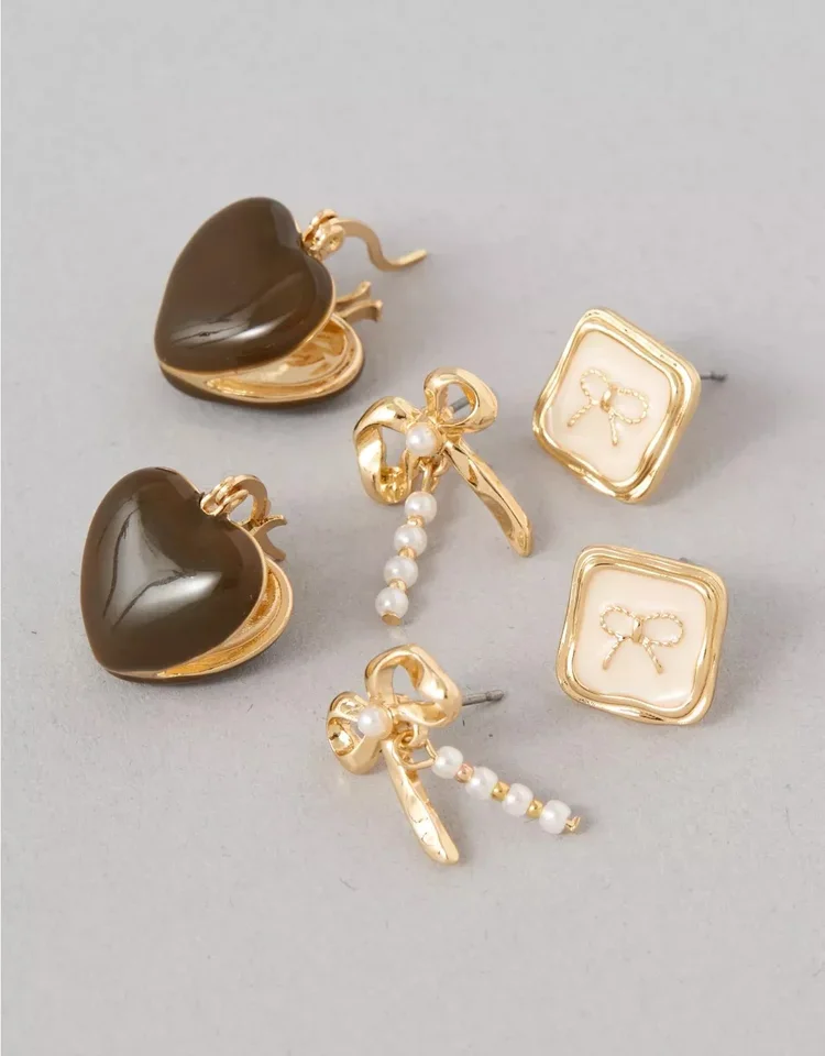 Three pairs of earrings: heart-shaped dark brown earrings with gold edges, square gold earrings with bows inside, and gold earrings with pearl and bow designs.