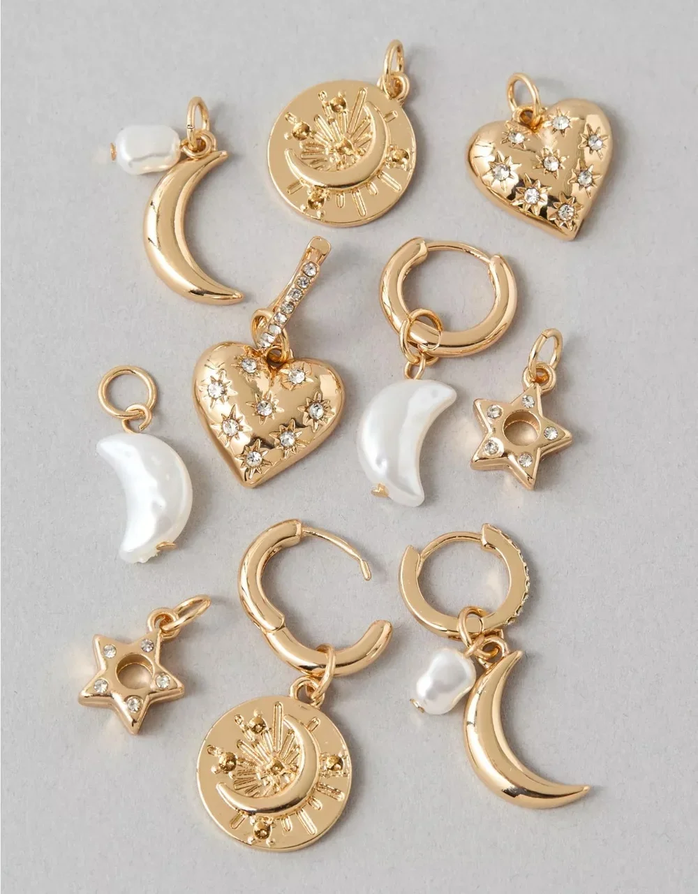 A collection of gold-colored charm pendants with moon, star, heart, and sun designs, some decorated with small white pearls and crystals.