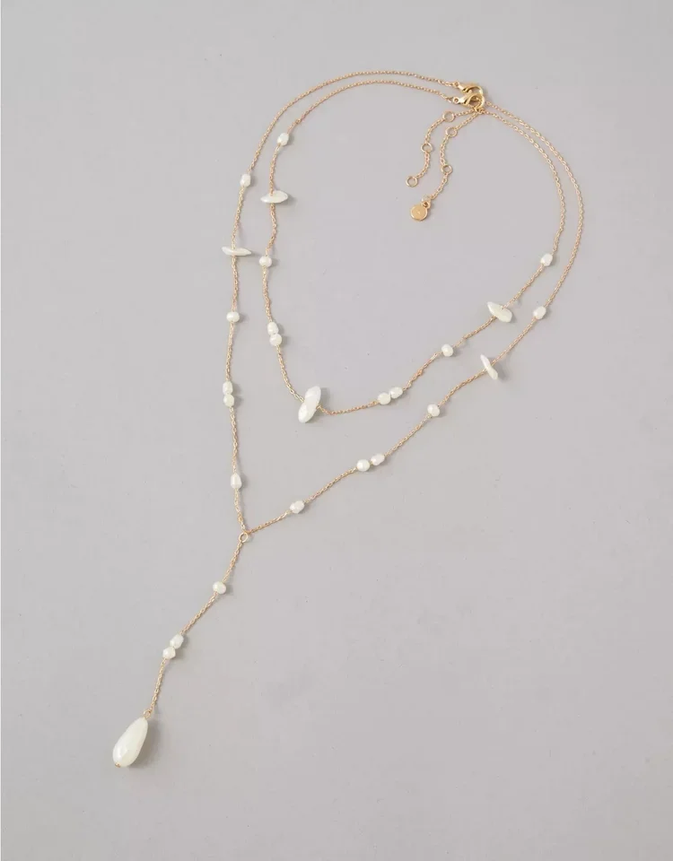 Elegant layered necklace with white beads and pendants on a light gray background.