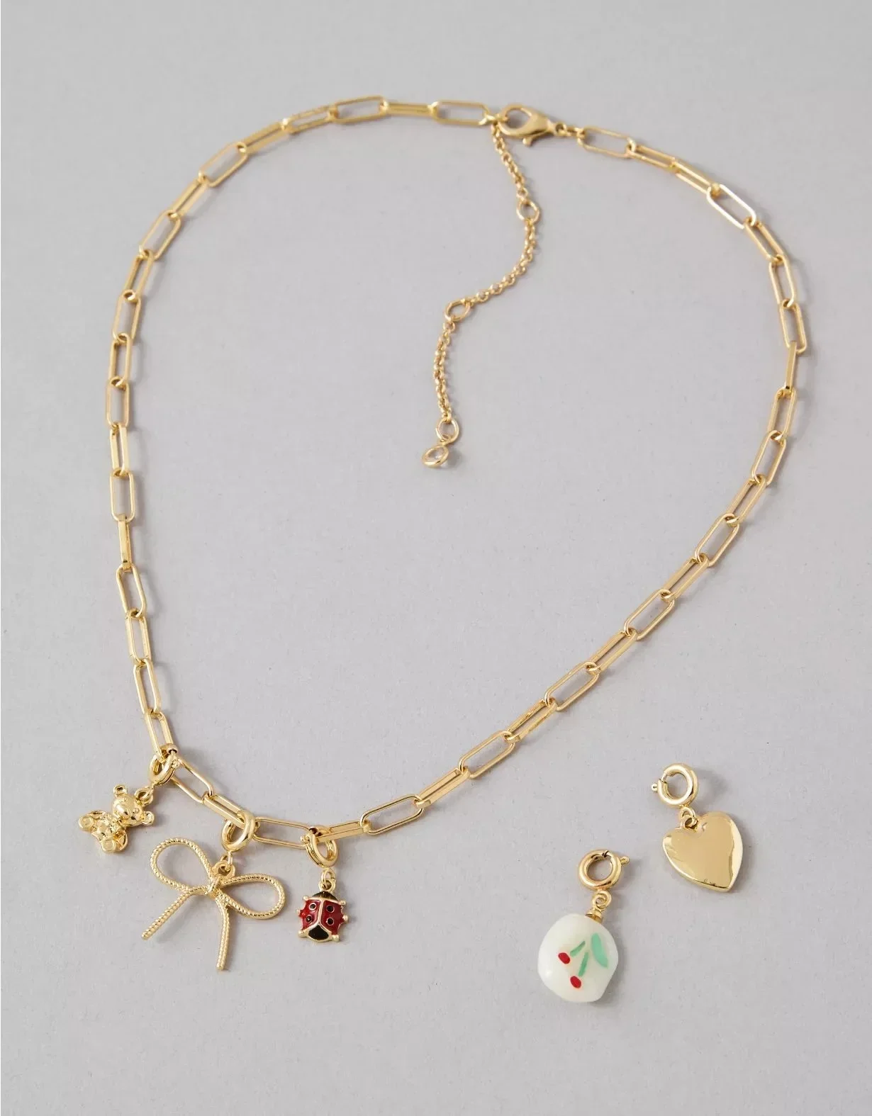 Gold chain necklace with charm pendants including a butterfly, ladybug, heart, and a charm with a cherry design, along with matching earrings with cherry design.
