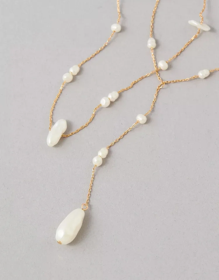 A gold chain necklace with multiple white pearl beads and two larger pearl pendant drops, displayed on a light gray background.