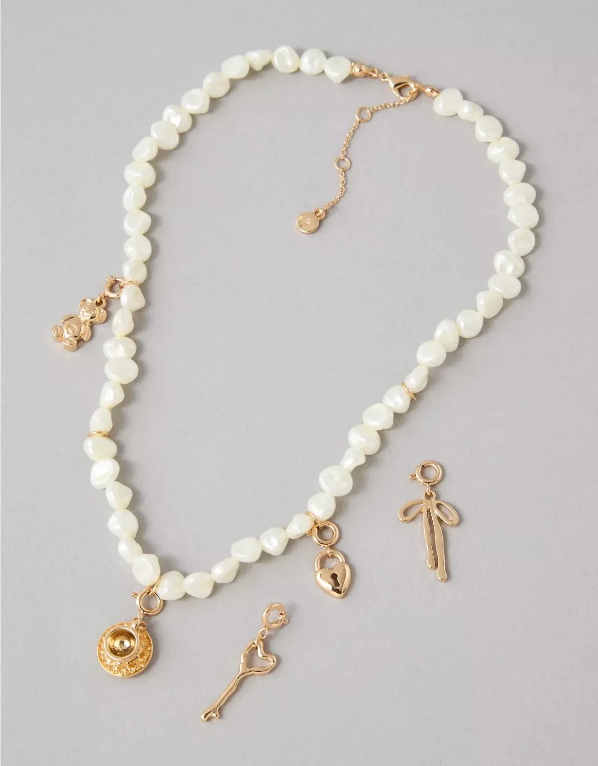 A pearl necklace with gold charms, including a lock, a key, and a boutique-shaped charm, laid on a grey surface.