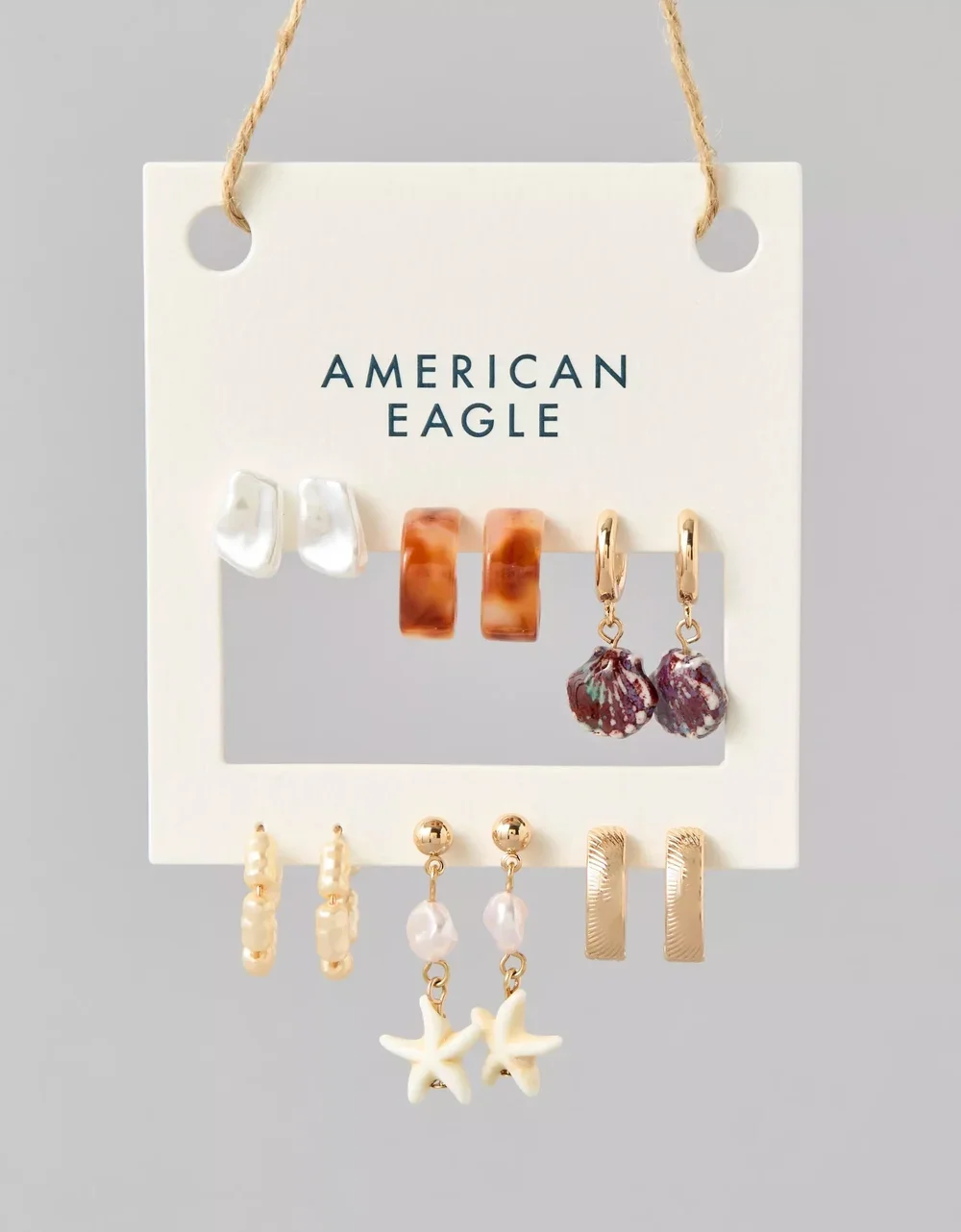 Display of nine pairs of earrings on a white card with 'American Eagle' printed in the center. The earrings include pearls, tortoiseshell, shells, gold bars, stars, and beads.