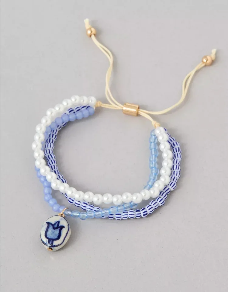 Beaded bracelet with white and blue beads, and a small oval charm featuring a blue tulip on a white background.