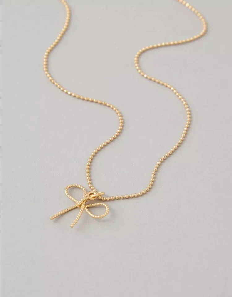 Gold beaded necklace with bow pendant on a light gray background.