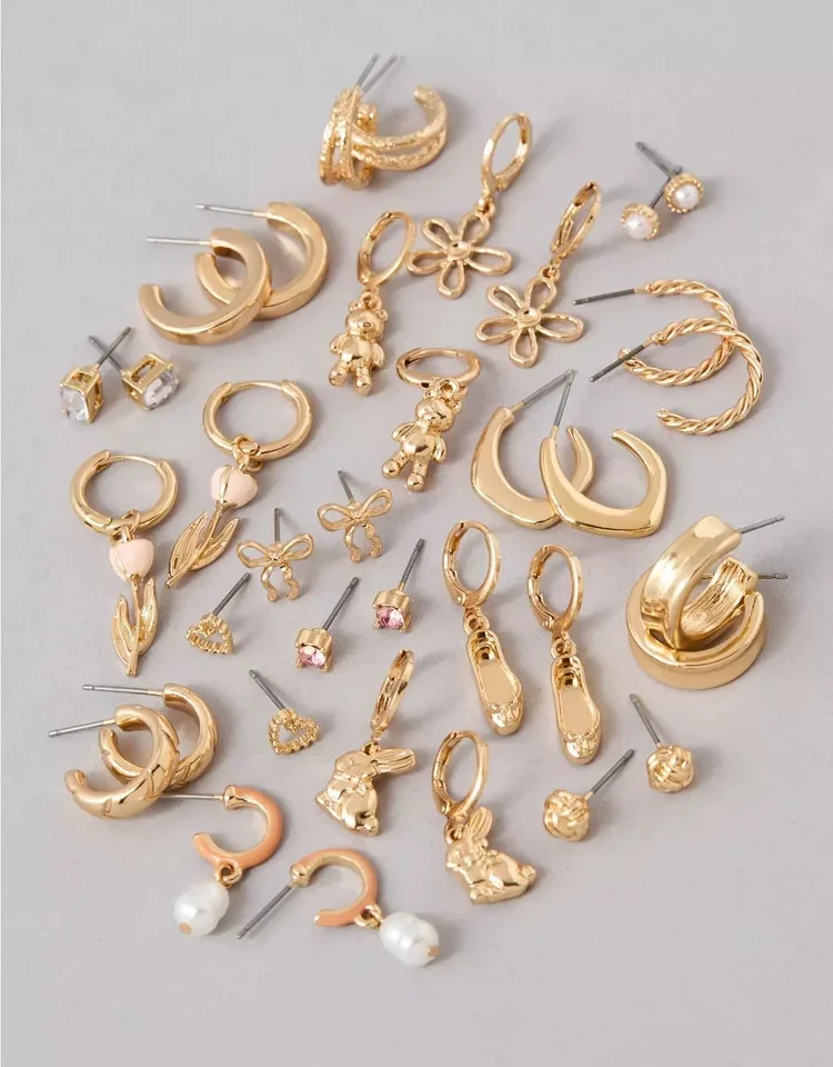An assortment of gold earrings, including hoops, studs, charms, and hoops with decorative elements, arranged on a light grey surface.