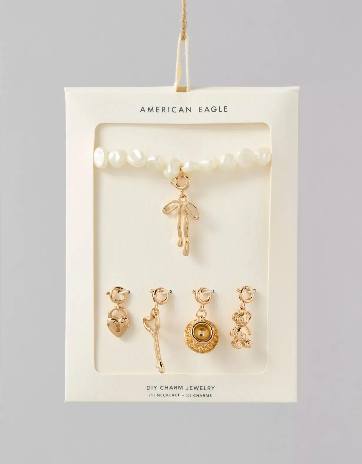 White jewelry display board with pearl necklace and five gold charms, labeled American Eagle, for DIY charm jewelry.