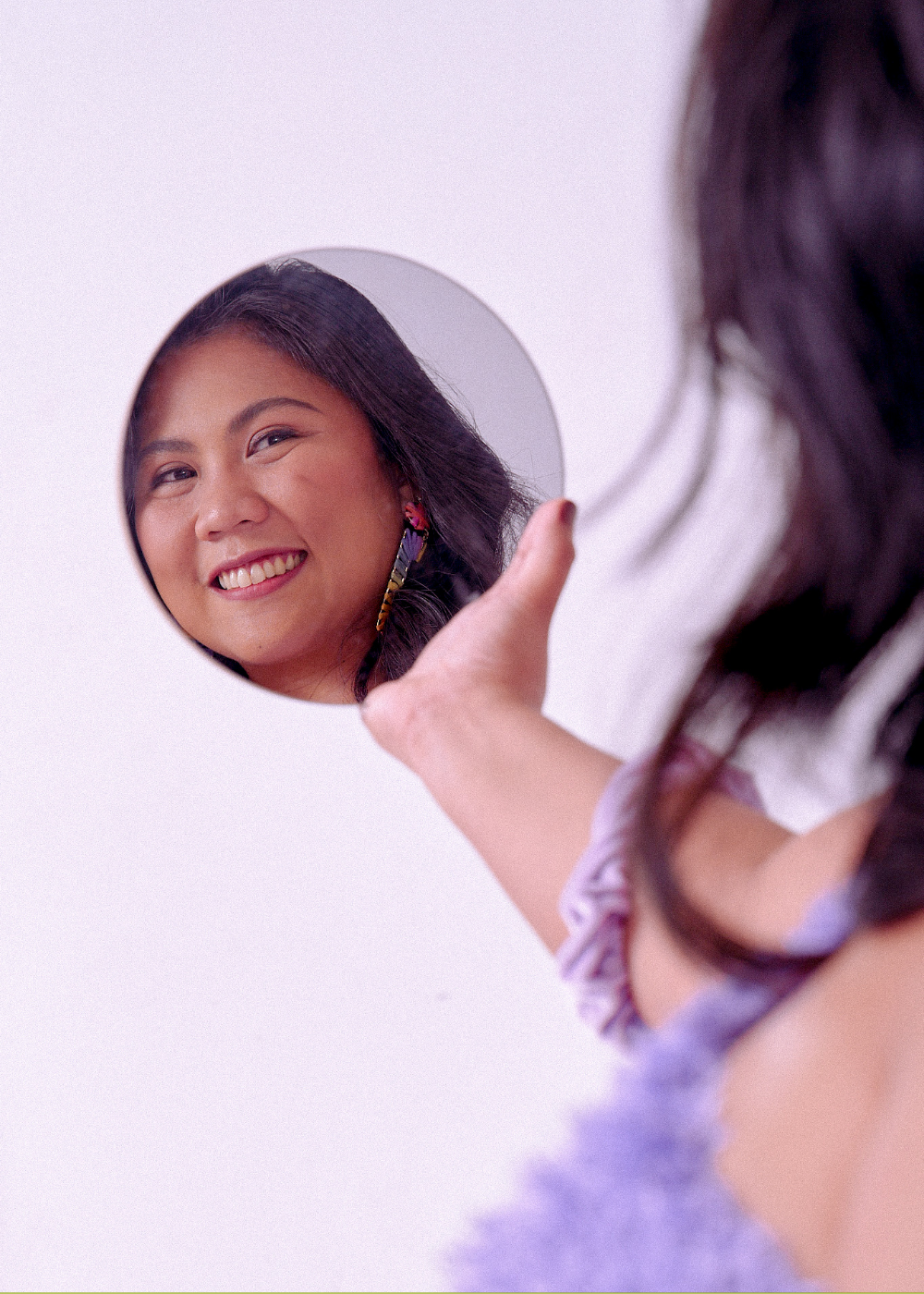 Woman holding a small mirror and smiling at her reflection.