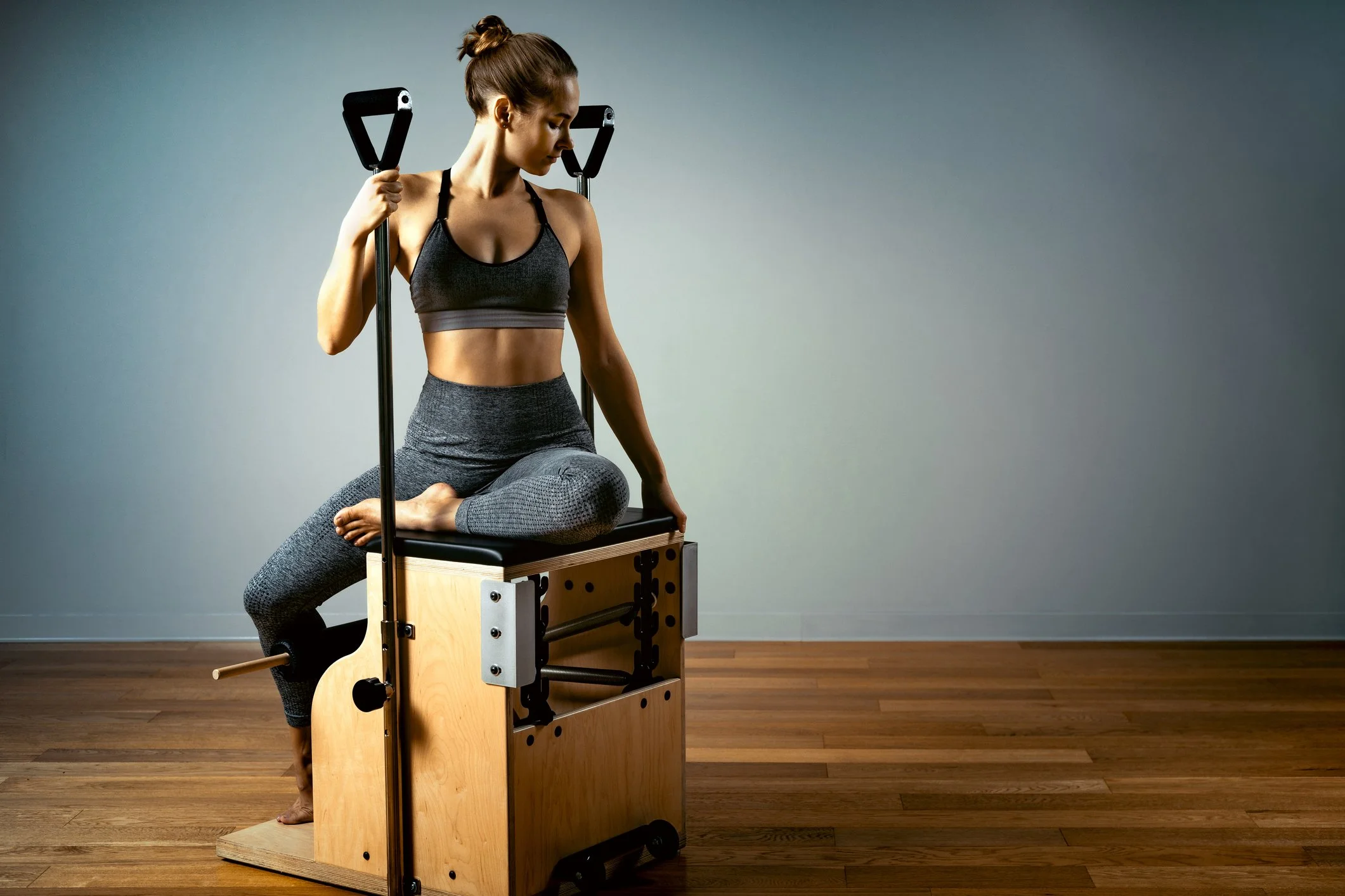 A woman in workout attire practicing yoga on a Pilates chair.