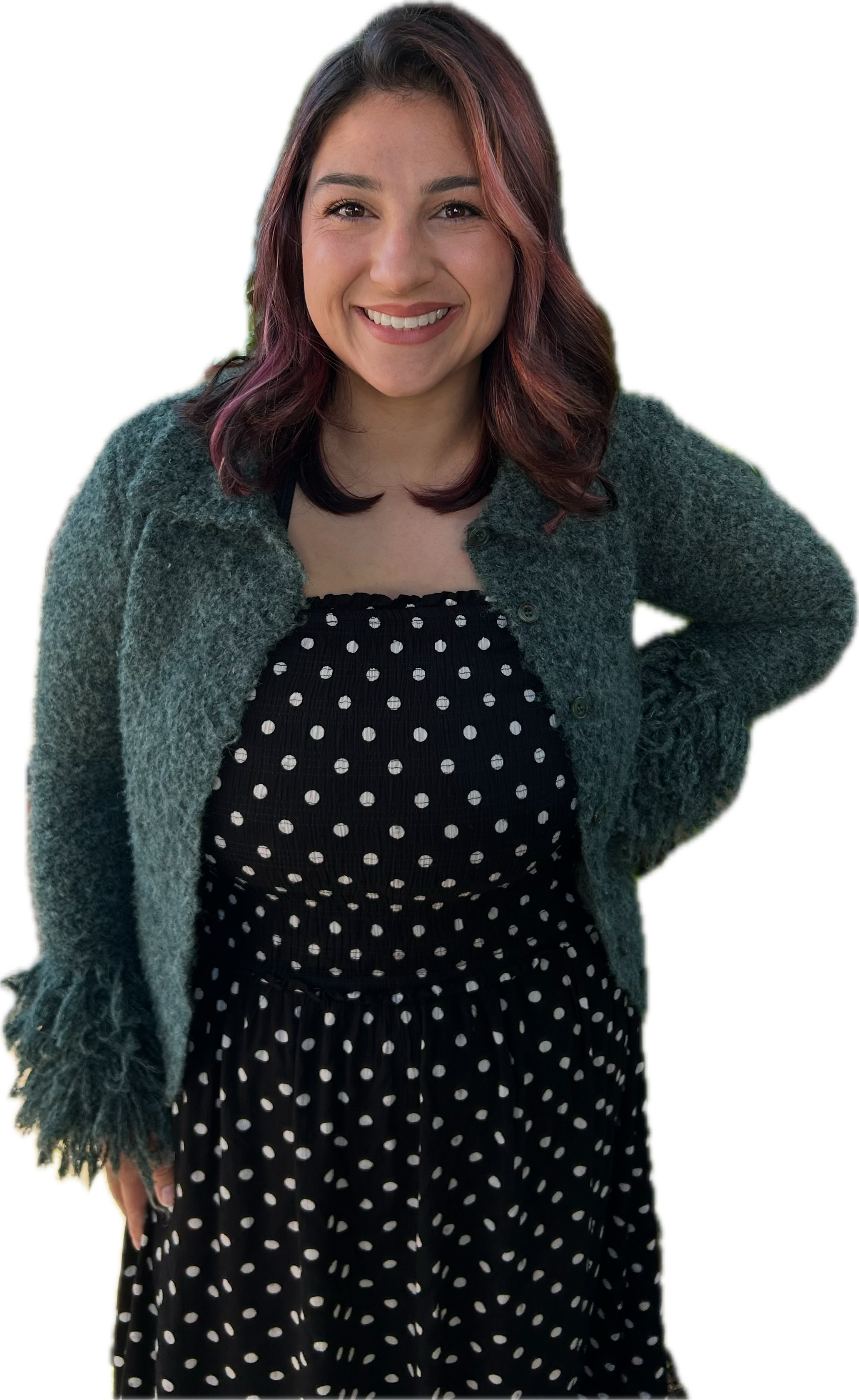 A woman with shoulder-length dark hair with reddish-brown highlights, smiling, wearing a dark polka dot dress and a gray cardigan with fringed edges.