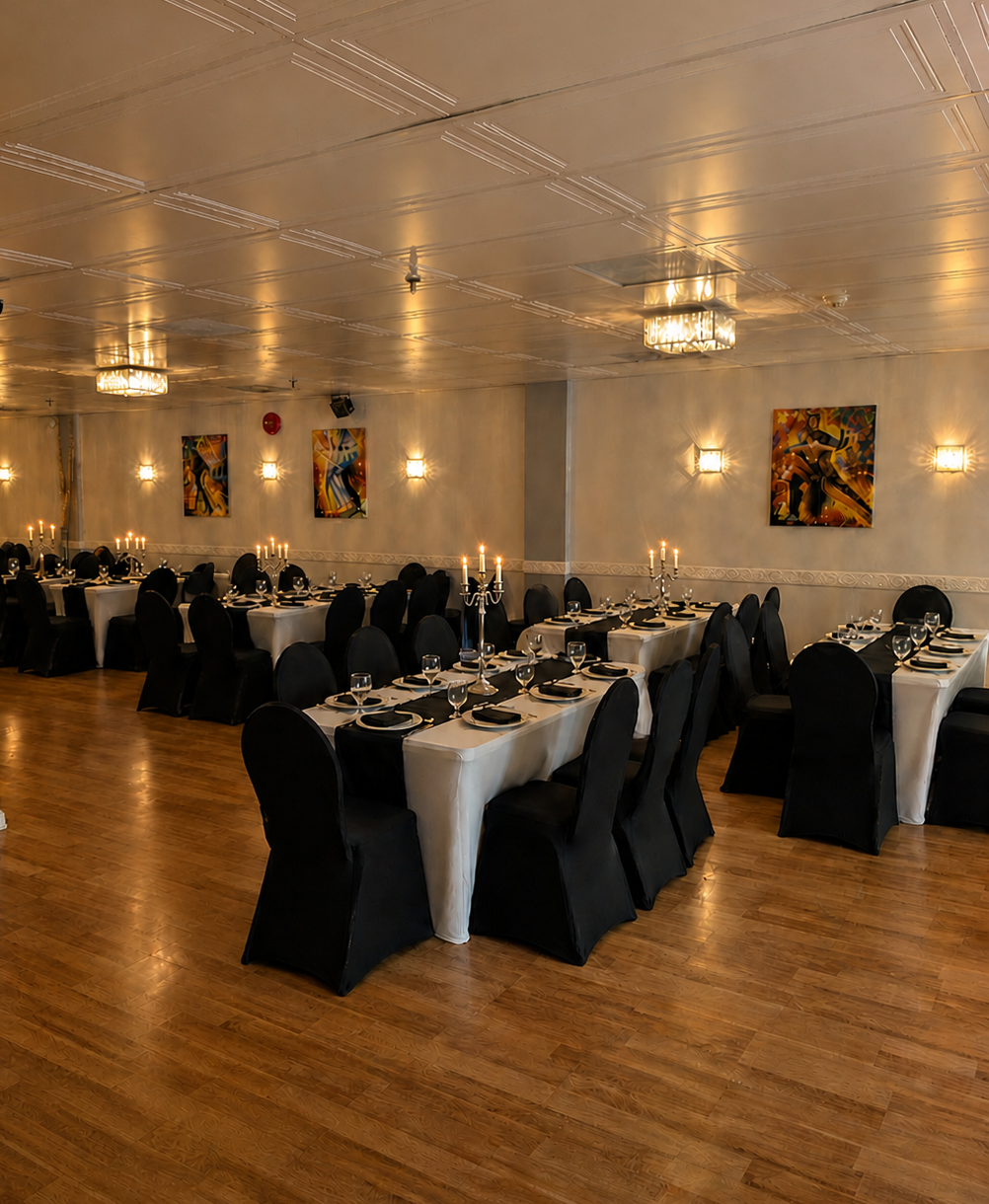 Elegant banquet hall decorated for a formal event with long tables covered in white tablecloths, black chairs, candelabras, and modern artwork on the walls.