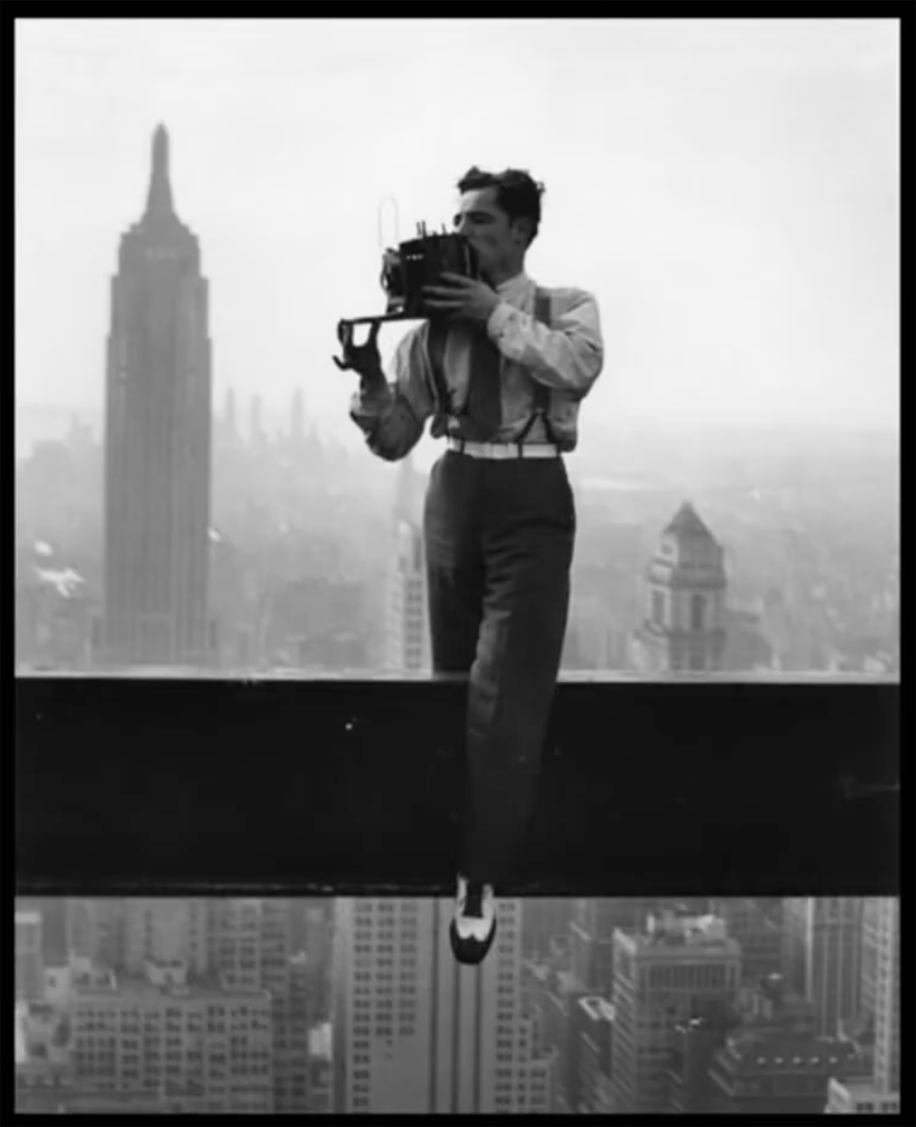 A black and white photo of a 1920s cinematographer recording film while standing on a high rise beam