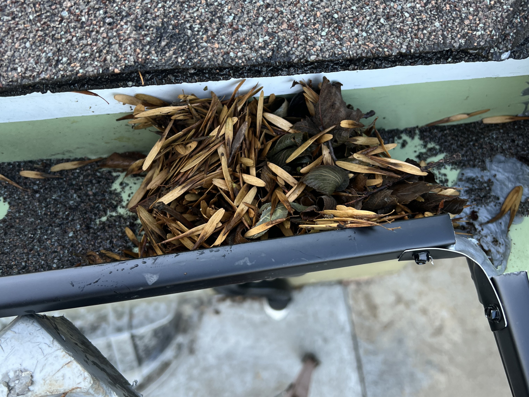 A close-up of a gutter filled with dry leaves, twigs, and small branches in the process of being cleaned out.
