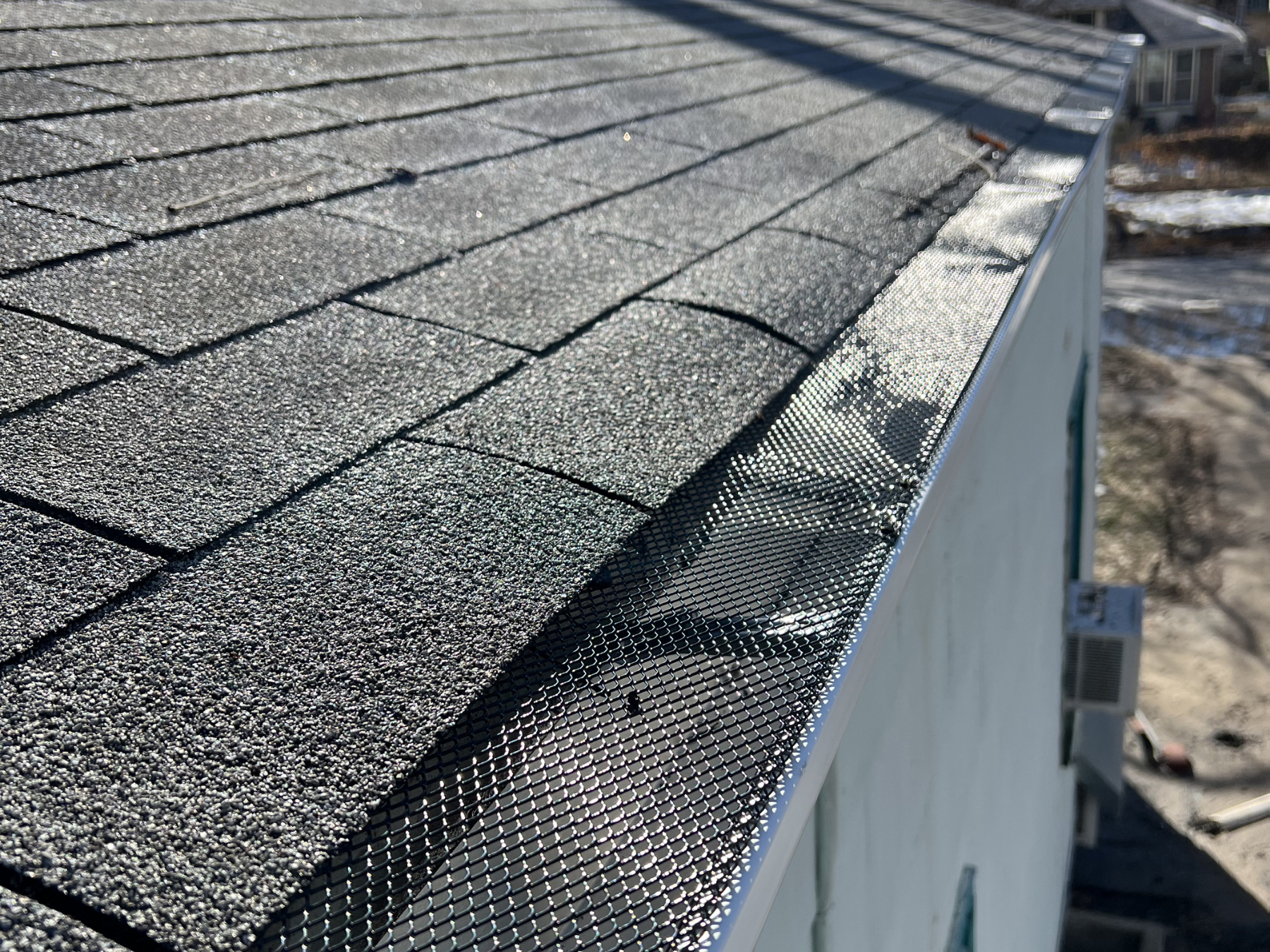 Close-up of a house's roof with asphalt shingles and a metal gutter guards installed by Gutter Solution LLC