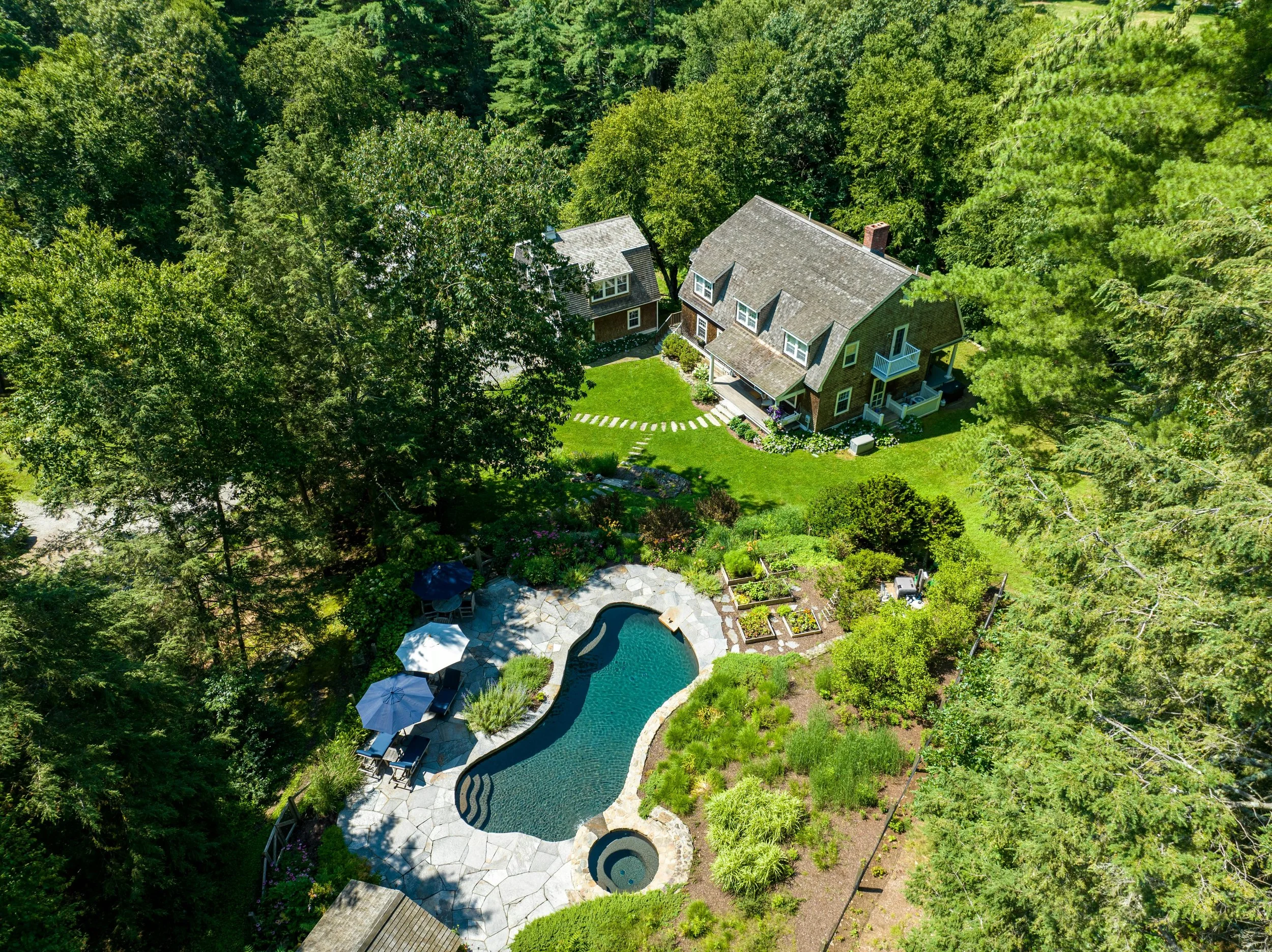 Aerial view of a house with a backyard, swimming pool, patio, and lush green trees surrounding the property.