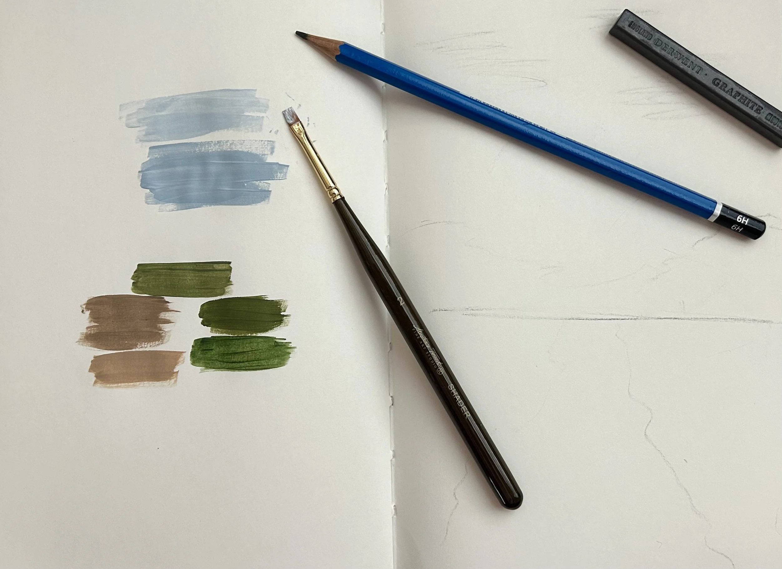 Open sketchbook with three paint swatches in blue, beige, and green, with a paintbrush and colored pencils resting on the page.