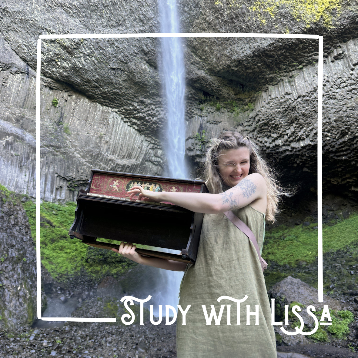 A woman with long curly hair and tattoos on her arm stands in front of a waterfall, holding a small piano and smiling.