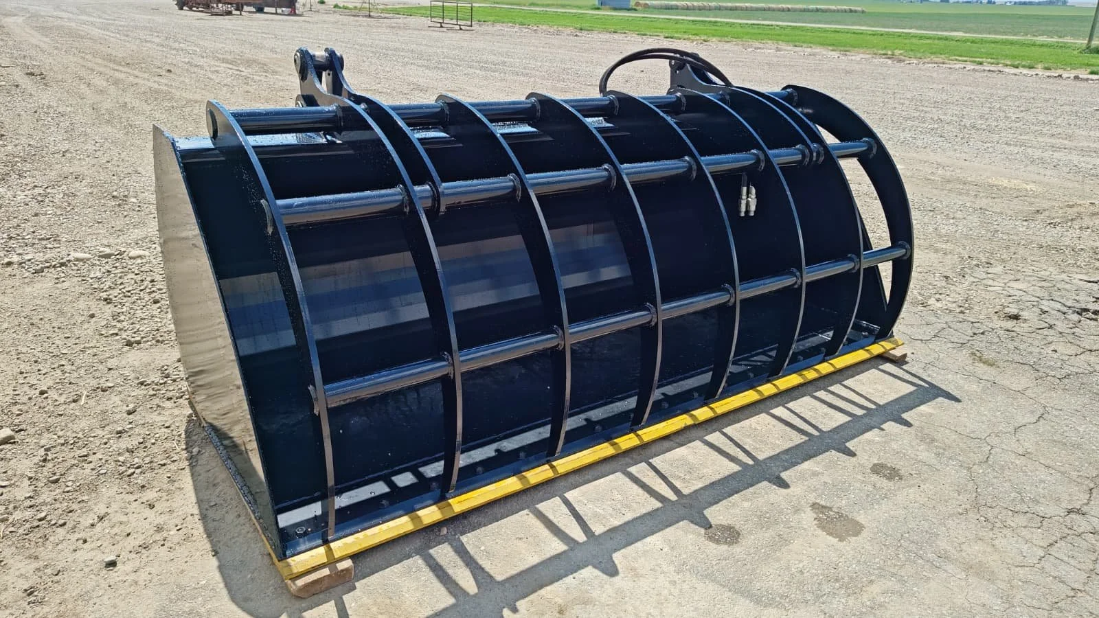 Large black metal construction attachment with curved bars and horizontal rods, placed on wooden blocks on a dirt ground