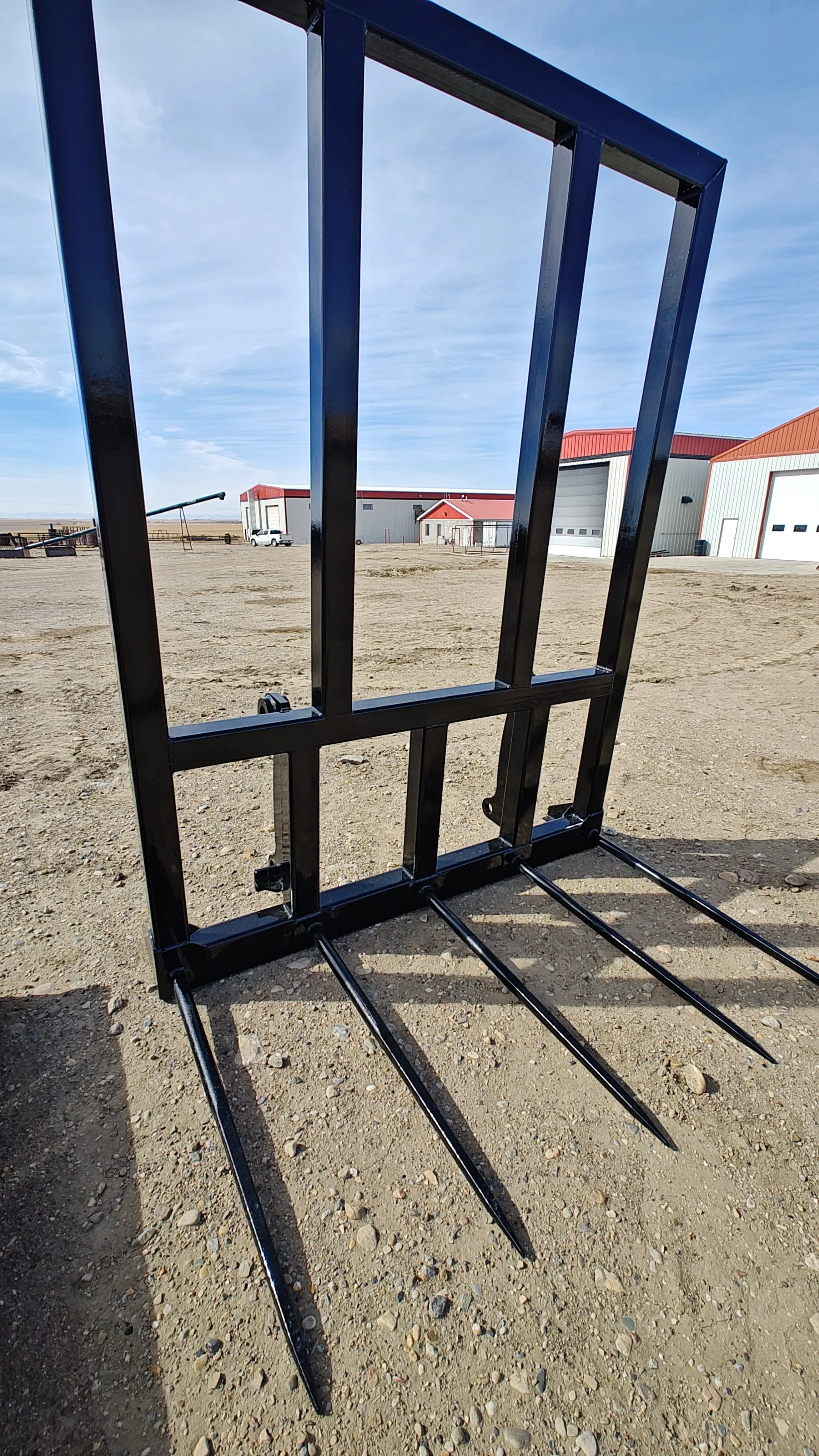 Black metal rack on a dirt surface with buildings and a blue sky in the background.