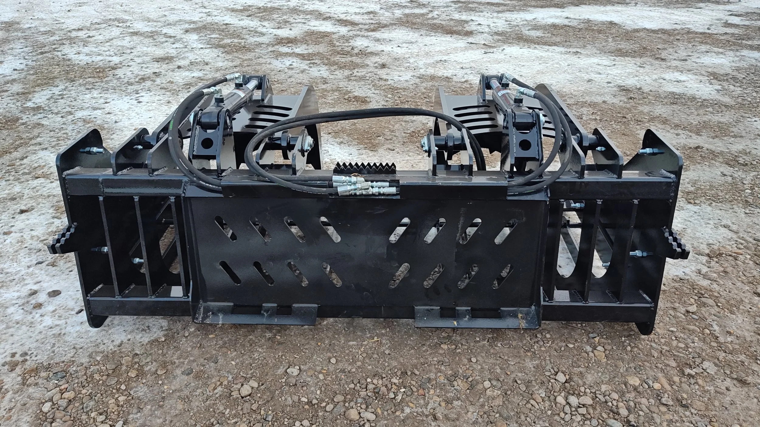 Metal machinery with hydraulic hoses and parts on a dirt ground.