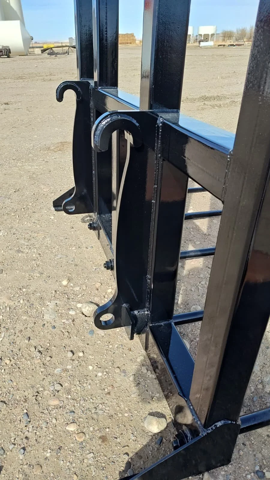 Close-up of a black metal fence or gate with decorative hooks, set on a gravel ground in an outdoor storage or construction area.